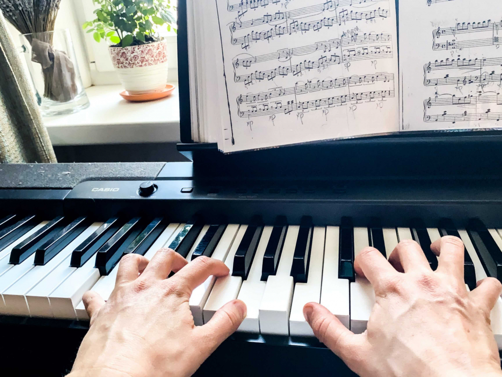 hands playing a digital keyboard with sheet music and a green plant