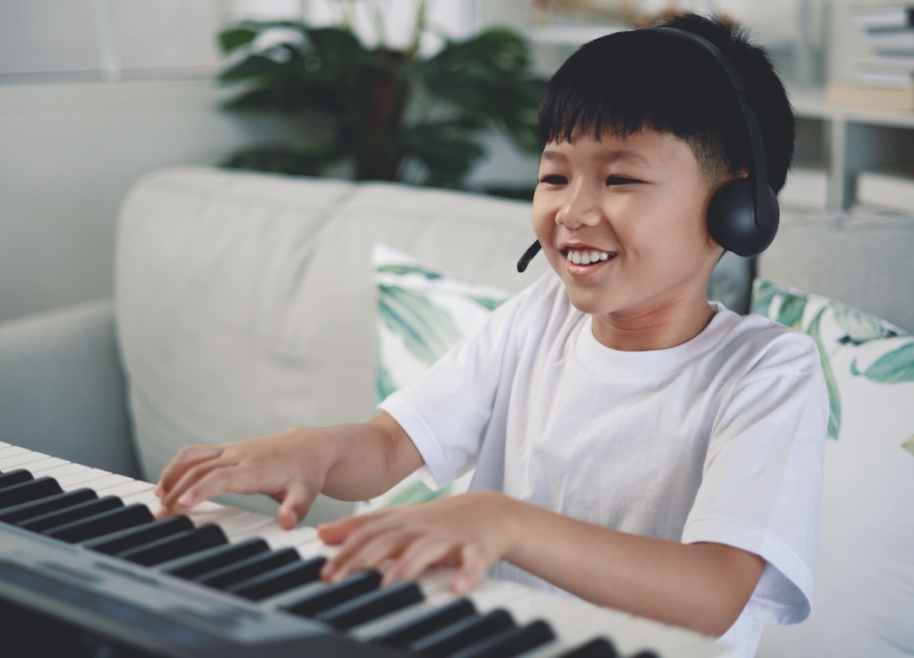 boy plays the piano with headphones on in an online lesson