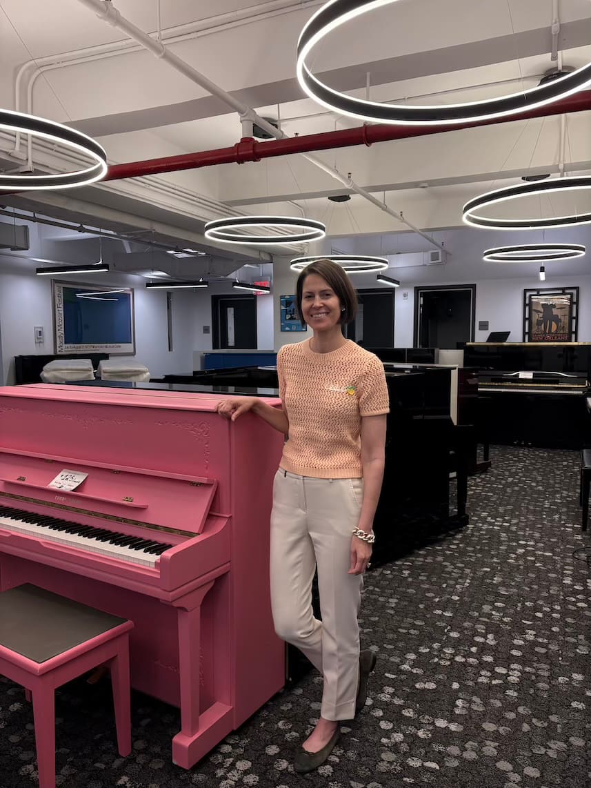 Photo of Sarah Binder, president of PianoPiano, standing next to a pink KPOP piano in their showroom.